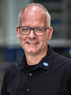 Mann in schwarzem Hemd lacht in die Kamera