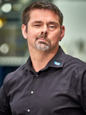 Mann in schwarzem Hemd guckt freundlich in die Kamera