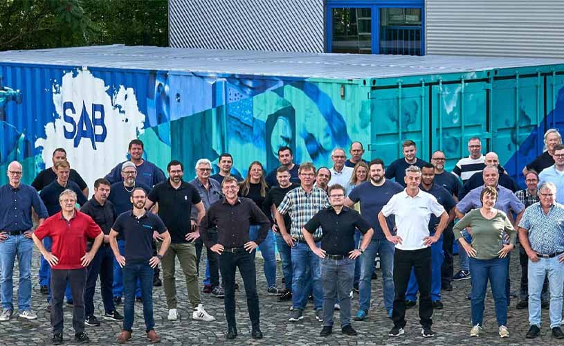 Viele Menschen stehen vor SAB-Gebaeude, Haende in die Hueften gestemmt