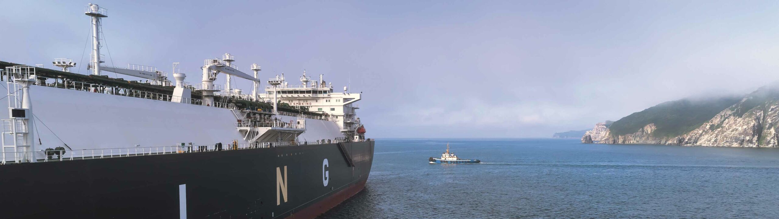 Grosses industrielles Schiff im Wasser, im Hintergrund huegelige Kueste
