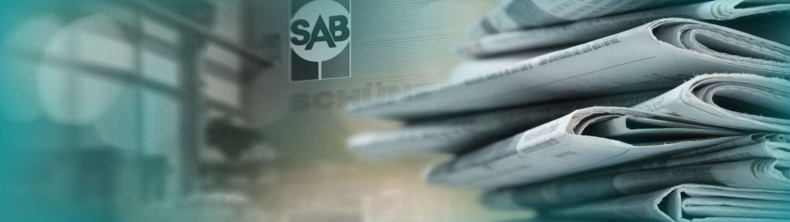 Stapel Zeitungen im Vordergrund, hinten SAB-Bremen Logo
